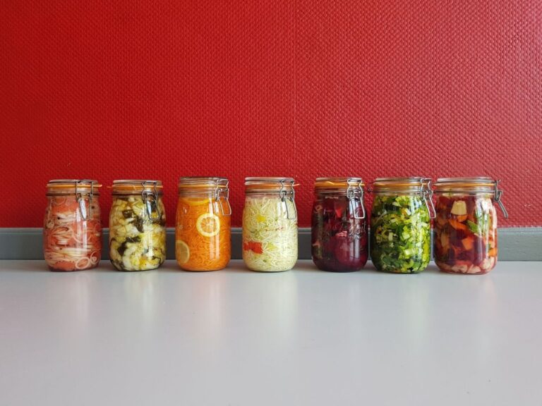 Seven glass jars of colorful vegetables arranged for fermentation