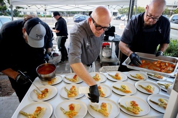 Chefs collaboratively plating multiple dishes beneath an outdoor canopy
