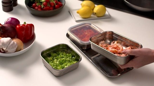 Stainless steel containers hold chopped vegetables and shrimp on a kitchen counter